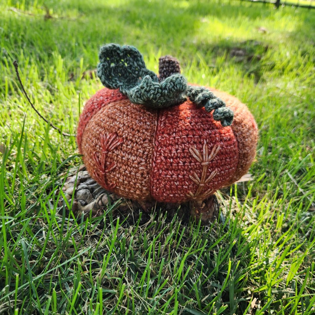 Crochet fall pumpkin shown at a side view in a garden